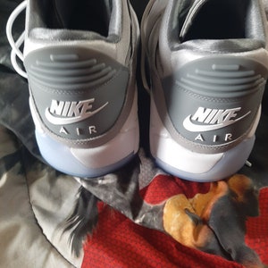 Puede incluir: Un par de zapatillas Nike Air grises y blancas con el logotipo de Nike y el texto "Air" en la parte posterior de cada zapato.