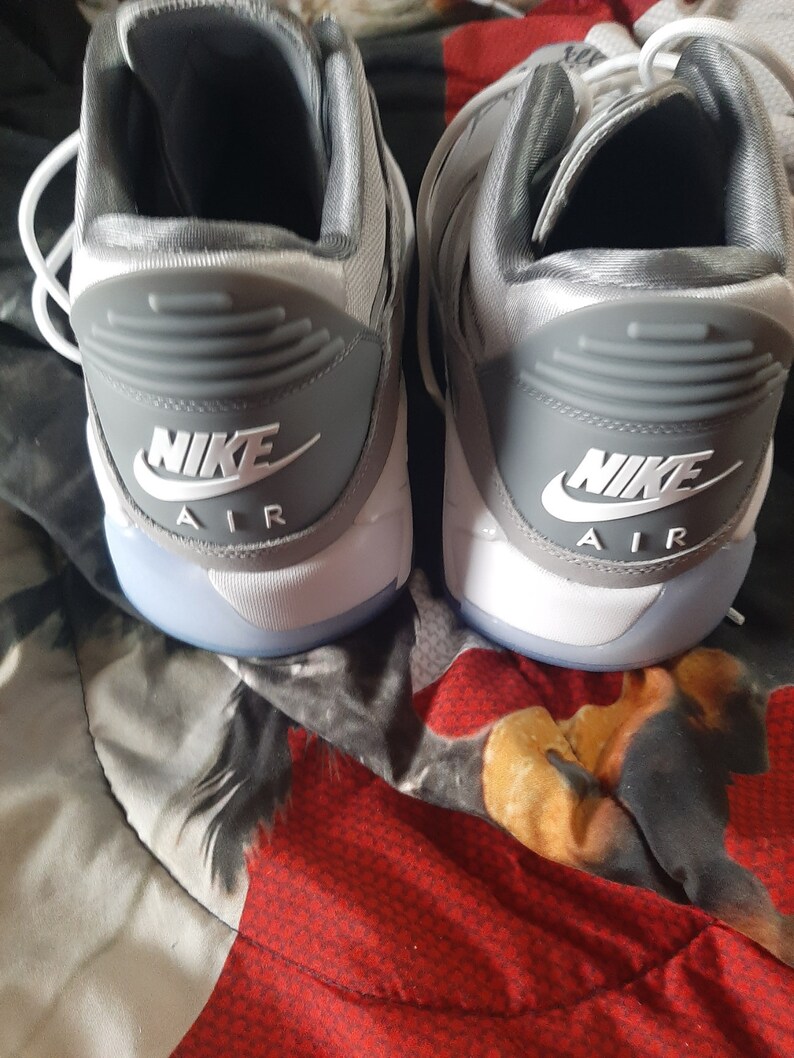Puede incluir: Un par de zapatillas Nike Air grises y blancas con el logotipo de Nike y el texto "Air" en la parte posterior de cada zapato.