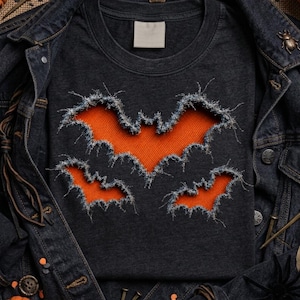 Puede incluir: Una camiseta gris carbón oscuro con tres recortes en forma de murciélago con bordes de mezclilla deshilachados, que revelan una tela acanalada de color naranja brillante debajo. La camiseta se coloca debajo de una chaqueta de mezclilla oscura.
