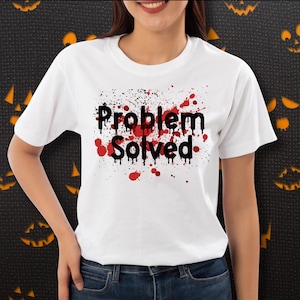 Puede incluir: Una camiseta blanca de manga corta con el texto negro "Problem Solved" centrado en el pecho. Las letras tienen un efecto de goteo y están rodeadas por un diseño de salpicaduras de pintura roja que imita gotas de sangre.