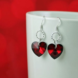 May include: Silver dangle earrings with red heart-shaped crystal accents.
