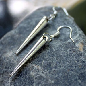 May include: A pair of silver earrings with a pointed, cone-shaped design. The earrings have a simple, minimalist style.