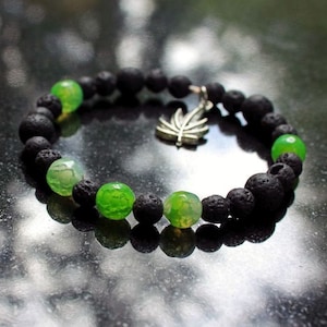 May include: A black lava rock and green agate beaded bracelet with a silver leaf charm.