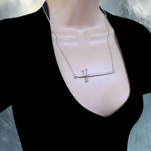 May include: A silver sword pendant necklace on a silver chain. The sword is a simple design with a cross guard and a pointed tip.