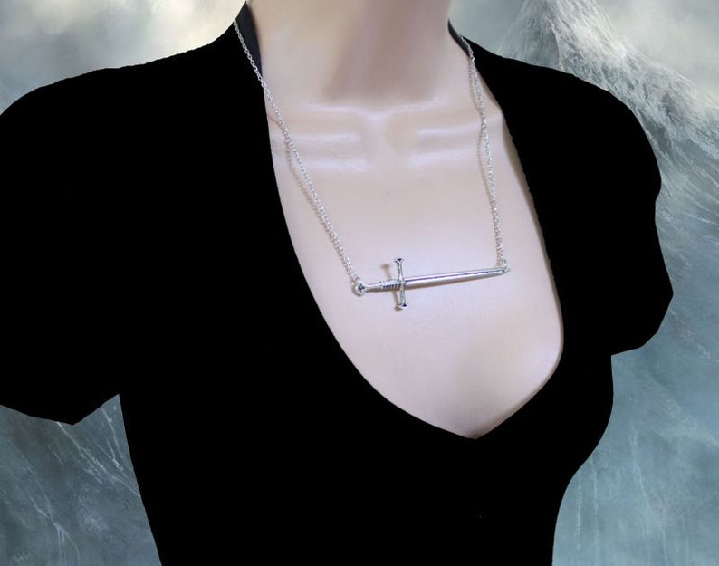May include: A silver sword pendant necklace on a silver chain. The sword is a simple design with a cross guard and a pointed tip.