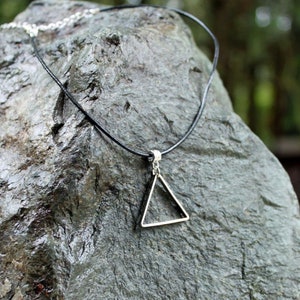 May include: A simple silver triangle pendant necklace on a black leather cord.