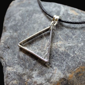 May include: A silver triangle pendant necklace on a black leather cord. The pendant is a simple geometric shape with a smooth, polished finish.