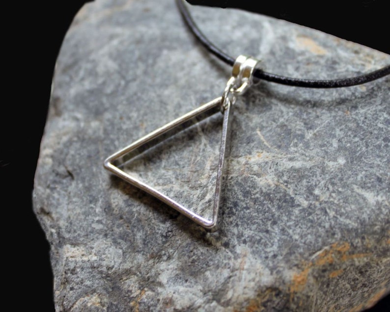 May include: A silver triangle pendant necklace on a black leather cord. The pendant is a simple geometric shape with a smooth, polished finish.