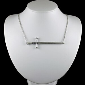 May include: A silver necklace with a sword pendant. The sword is a simple design with a cross guard and a pointed tip.