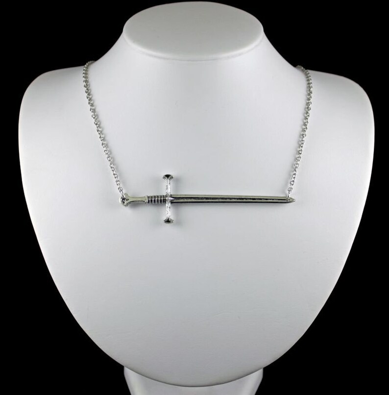 May include: A silver necklace with a sword pendant. The sword is a simple design with a cross guard and a pointed tip.