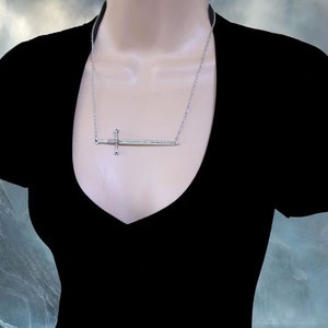 May include: A silver sword pendant necklace. The sword is a simple design with a cross guard and a pointed tip. The necklace is on a silver chain.