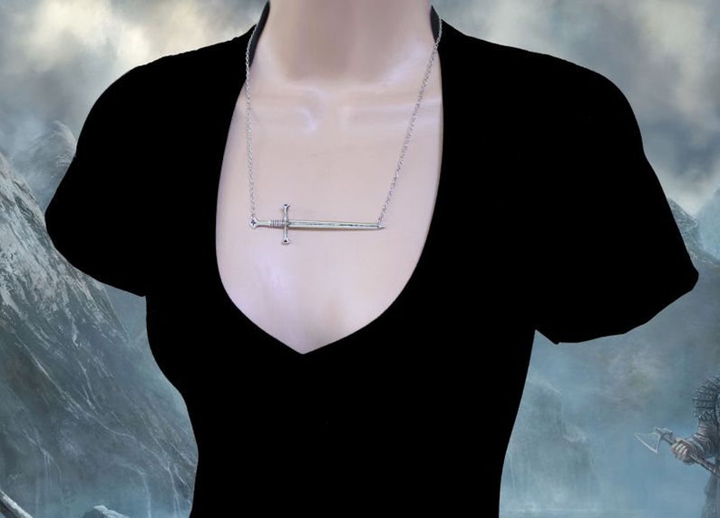 May include: A silver sword pendant necklace. The sword is a simple design with a cross guard and a pointed tip. The necklace is on a silver chain.