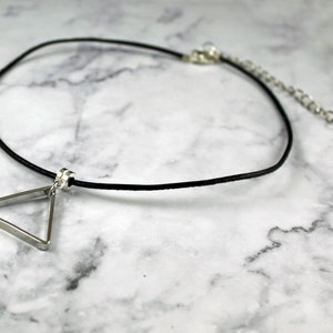 May include: A silver triangle pendant necklace with a black leather cord. The necklace has an adjustable clasp.