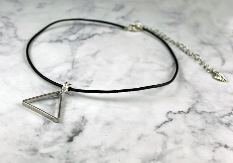 May include: A silver triangle pendant necklace with a black leather cord. The necklace has an adjustable clasp.