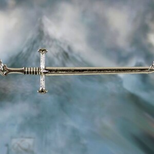 May include: A silver sword pendant necklace with a chain. The sword has a detailed design and is suspended from a silver chain.