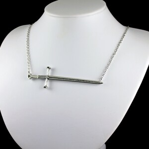 May include: A silver necklace with a sword pendant. The sword is a simple design with a pointed tip and a cross guard.