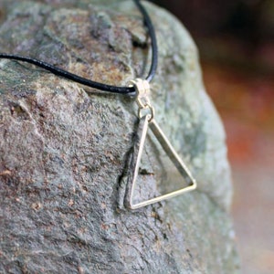 May include: A silver triangle pendant necklace with a black cord. The pendant is a simple, geometric shape with a smooth finish.