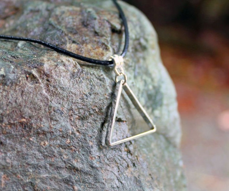 May include: A silver triangle pendant necklace with a black cord. The pendant is a simple, geometric shape with a smooth finish.