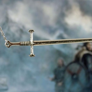 May include: A silver sword pendant necklace with a detailed design. The sword is suspended from a silver chain.