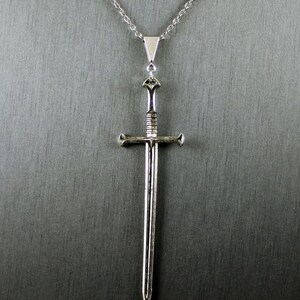K&ouml;nnte beinhalten: Eine silberne Schwertkette mit Kette. Das Schwert hat eine spitze Spitze und einen Kreuzschutz.