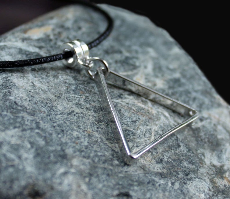 May include: A silver triangle pendant necklace with a black cord. The pendant is a simple geometric shape with a smooth, polished finish.