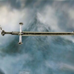 May include: A silver sword pendant necklace with a chain. The sword has a simple design with a cross guard and a pointed tip.