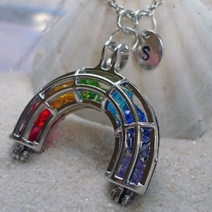 May include: A silver rainbow charm necklace with a colorful glass inlay. The necklace has a silver initial charm with the letter "S" on it.