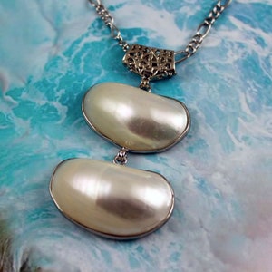 May include: A silver chain necklace with a delicate filigree pendant and two large, white, oval-shaped pearls.