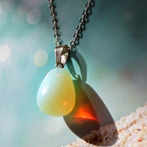 May include: A silver chain necklace with a teardrop-shaped opal pendant. The opal is a milky white color with a hint of yellow.