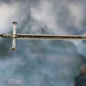 May include: A silver sword pendant necklace. The sword is a simple design with a cross guard and a pointed tip. The necklace is on a silver chain.