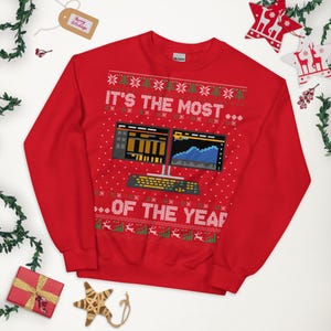 Peut inclure: Sweat-shirt rouge sur le thème de Noël avec le texte "IT'S THE MOST... OF THE YEAR" et un graphique d'écran d'ordinateur. Le motif comprend des flocons de neige, des sapins de Noël et des rennes. Une étiquette "Merry Holidays" est visible.