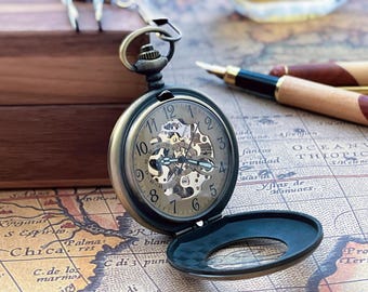 May include: Antique-style pocket watch with a skeleton dial, showcasing the intricate inner workings. The watch has a dark metal casing and is open, revealing the time. It rests on a vintage map, with pens in the background.