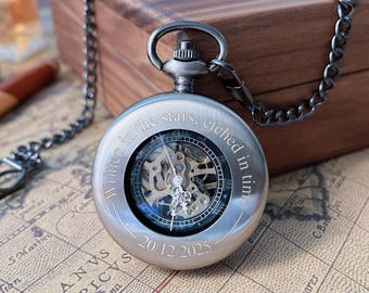 May include: Silver pocket watch with a visible mechanical movement. The watch has a chain and is engraved with the words "Written in the stars, etched in time" and the date 20/12/2025. The watch is set against a wooden box and a map.