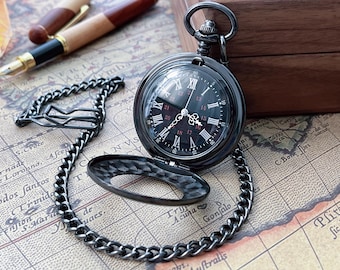 May include: A black pocket watch with a chain, open to reveal a black face with white Roman numerals. The watch rests on a map, with a pen and wooden box in the background.