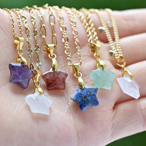 May include: A collection of gold-colored chain necklaces, each featuring a star-shaped gemstone pendant. The pendants are various colors, including purple, red, blue, and green. The necklaces are displayed against a blurred background.