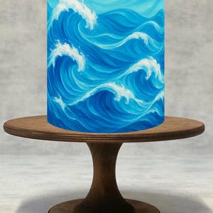 Può includere: Un oggetto cilindrico con un disegno di onde oceaniche dipinte, in tonalità di blu e bianco, è posto su un piccolo supporto rotondo di legno per torte. Le onde sono raffigurate con creste bianche e acqua blu vorticosa.