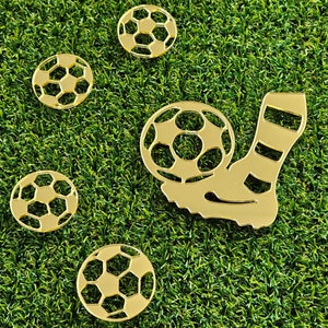Könnte beinhalten: Goldfarbene Fußball-Themen-Ausschnitte auf einer grünen Oberfläche. Das Design umfasst fünf Fußbälle und den Fuß eines Fußballspielers, der einen Ball tritt. Die Ausschnitte sind auf einem grünen, kunstrasenartigen Hintergrund angeordnet.