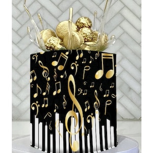 May include: A cake decorated with a musical theme, featuring a black base with gold musical notes and a piano key design. The cake is topped with gold spheres and decorative elements. The cake is presented on a white cake stand.