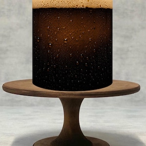 Peut inclure: Un objet cylindrique présentant un liquide brun foncé avec des gouttelettes de condensation sur la surface extérieure et une épaisse couche de mousse beige clair au sommet, posé sur un socle en bois circulaire avec un pied central.