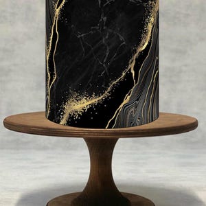 May include: A cylindrical object with a black marble design and gold veining sits on a wooden cake stand. The marble pattern has a luxurious appearance, with gold accents that add a touch of elegance. The cake stand is made of dark wood.