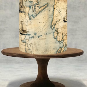 Peut inclure: Un contour de gâteau cylindrique présentant un motif de carte marine ancienne avec des tons parchemin beige, des côtes bleues et des illustrations à l'encre noire de voiliers. La carte inclut des lignes de navigation et des textes.