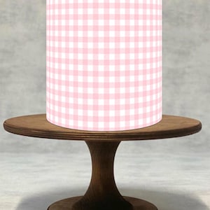 Op de afbeelding: Een cilindrische taartwikkel met een lichtroze en wit gingham ruitpatroon. De wikkel staat op een donkerbruine houten taartstandaard met een rond blad en een voetstuk, wat zorgt voor een strak en eenvoudig ontwerp voor de presentatie.