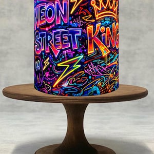 Peut inclure: Un objet cylindrique avec les mots "NEON STREET KING" dans un design de style graffiti, avec des couleurs néon et une couronne. L'objet est présenté sur un petit présentoir à gâteau rond en bois.