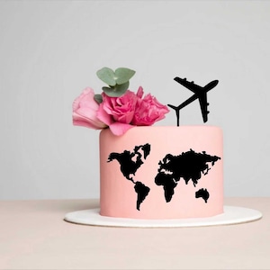 Puede incluir: Un pastel rosa decorado con un mapa del mundo negro y un adorno de avión, coronado con rosas rosas y vegetación. El pastel está sobre un soporte blanco, perfecto para una celebración temática de viajes.