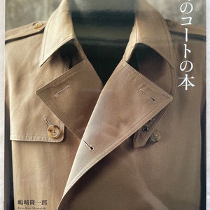 Puede incluir: Una gabardina marrón con cuello abotonado y dos botones en la parte delantera. El texto "男のコートの本" está impreso en el lado derecho de la imagen. El texto "嶋崎隆一郎 Ryuichiro Shimazaki" está impreso debajo de la gabardina. El texto "S, M, L, XLの実物大ダーンつき" está impreso debajo del nombre del autor. El texto "文化出版局" está impreso en la esquina inferior derecha de la imagen.