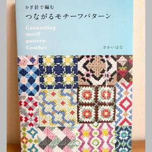 Op de afbeelding: Een boek getiteld "Connecting Motif Pattern Crochet" met Japanse tekst. De omslag heeft een lichtblauwe achtergrond en een collage van kleurrijke haakpatronen. Het boek is van Pomadour's Craft.