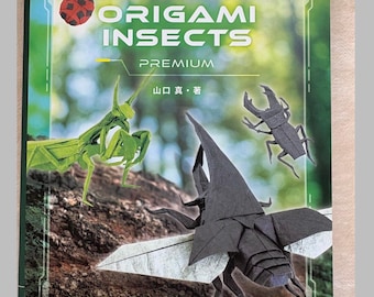 May include: A book titled Origami Insects Premium by Makoto Yamaguchi featuring a green praying mantis, a black beetle, a red ladybug, and a brown rhinoceros beetle on the cover against a blurred forest background with white text.