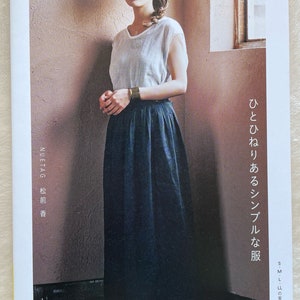 May include: A book cover featuring a woman wearing a white sleeveless shirt, a wide-brimmed straw hat, and a dark blue skirt. The text on the cover reads "NUETAG 松前香" and "ひとひねりあるシンプルな服".