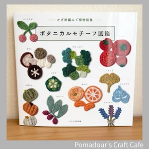 以下が含まれることがあります： 「ボタニカルモチーフ図鑑」というタイトルの本。さくらんぼ、きのこ、ブロッコリー、トマト、オレンジなど、様々な野菜や果物の編み物パターンが掲載されています。表紙は白で、日本語のテキストとカラフルな編み物デザインが特徴です。