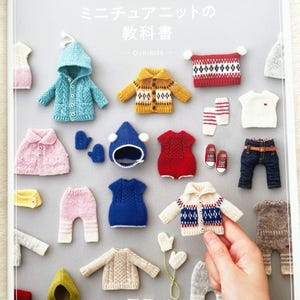 May include: A book titled "DOLL KNIT BOOK 1/12ドールサイズのミニチュアニットの教科書 - Ochibits -" featuring a selection of knitted miniature clothing items, such as sweaters, hats, trousers, and shoes.
